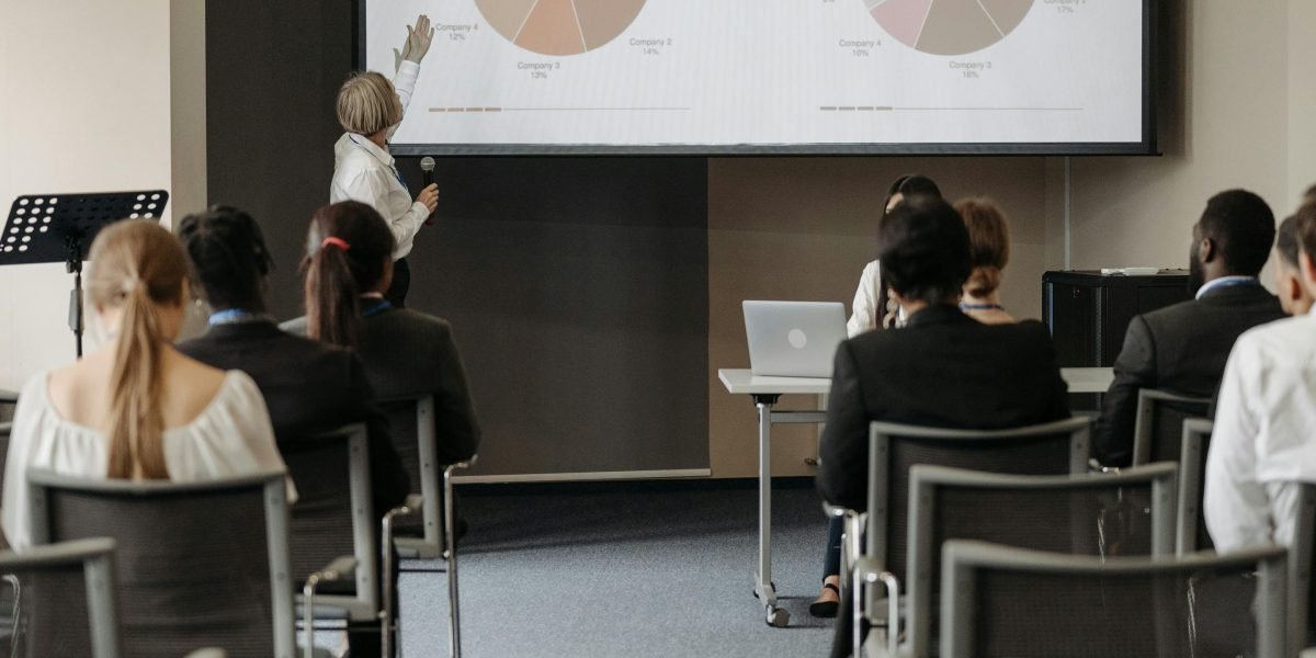 A person confidently presenting data on a large screen to a small group, symbolizing audience analysis and strategic alignment.